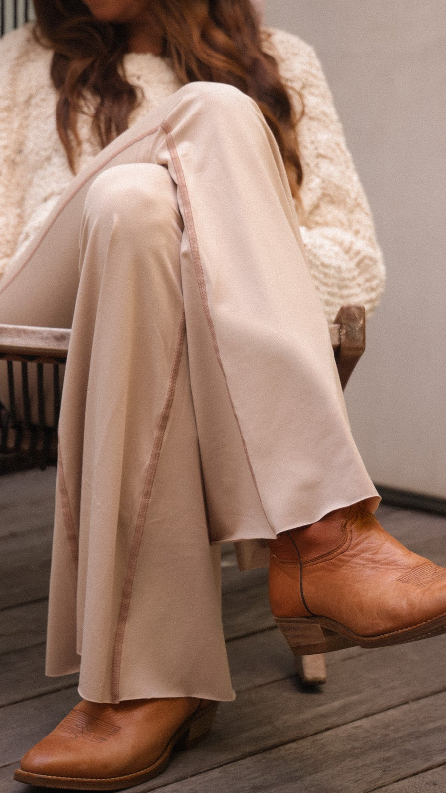 Person wearing beige pants and brown boots sitting on a wooden chair.